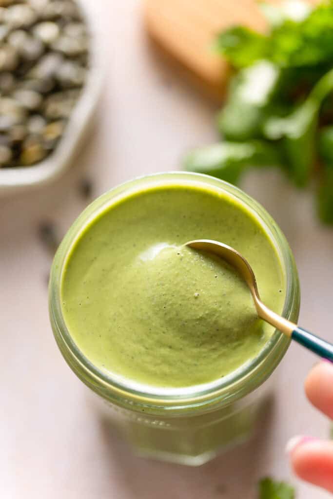 a spoon stirring Cilantro Pepita Dressing in a jar