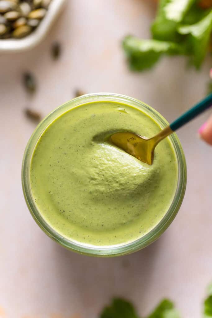 a small spoon full of cilantro pepita dressing over a jar