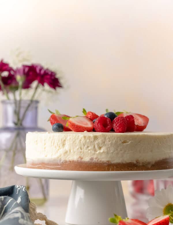 gluten free no bake cheesecake on a cake stand with fresh berries on top