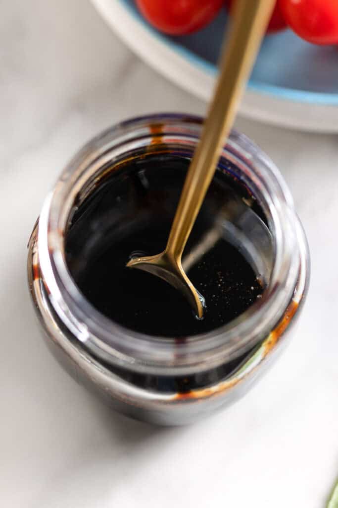 Homemade balsamic glaze in a small jar with spoon inside