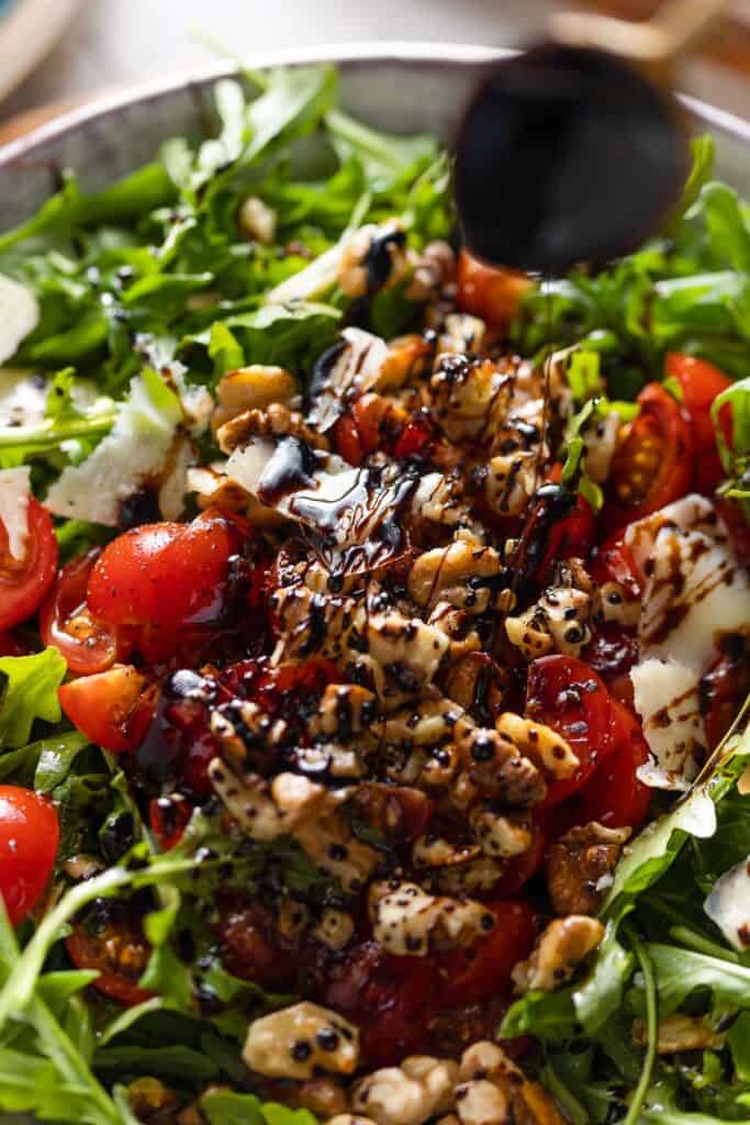 a balsamic glaze drizzling over a Tomato Arugula Salad with chopped walnuts and shaved parmesan