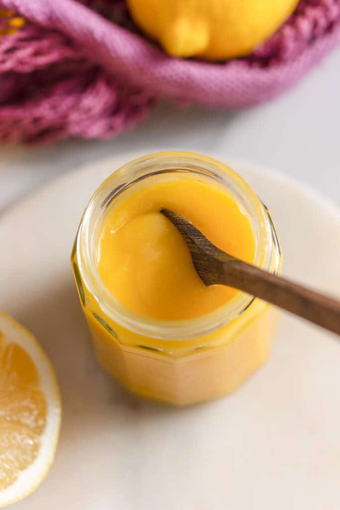 homemade lemon curd in a storage jar with a wooden spoon