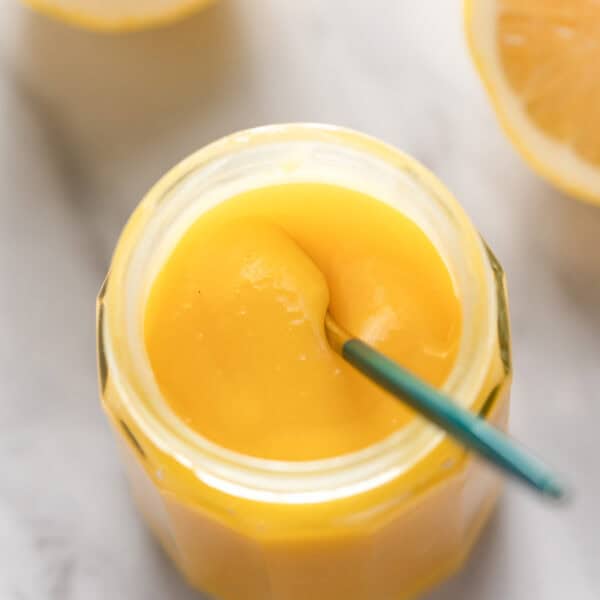 homemade lemon curd in a storage jar with small spoon stirring the curd