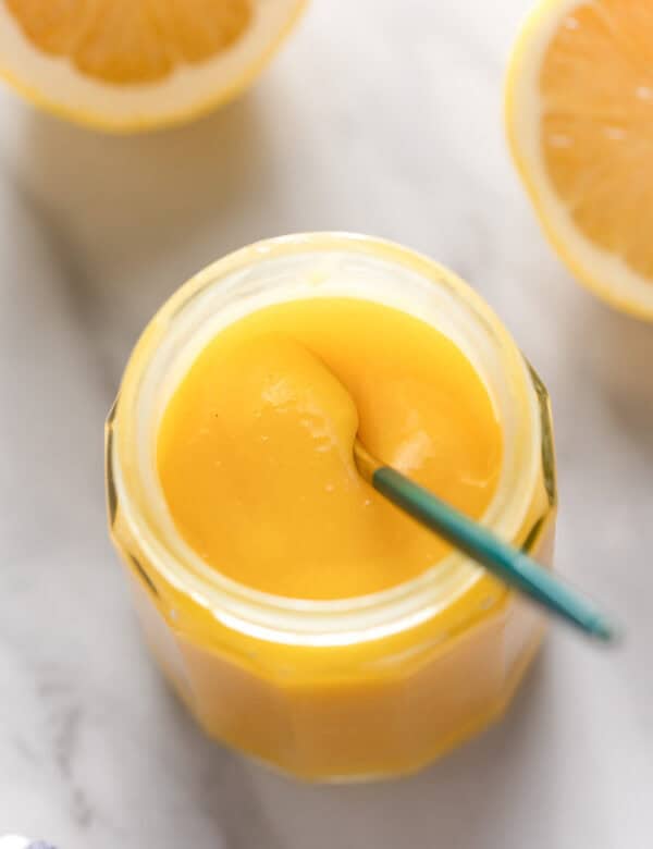 homemade lemon curd in a storage jar with small spoon stirring the curd