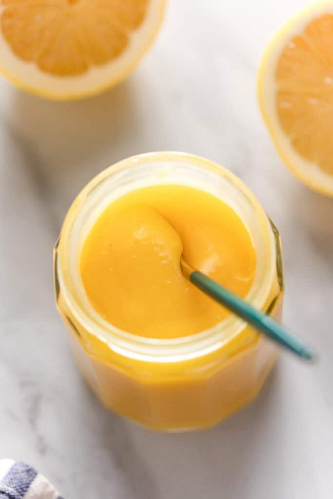 homemade lemon curd in a storage jar with small spoon stirring the curd