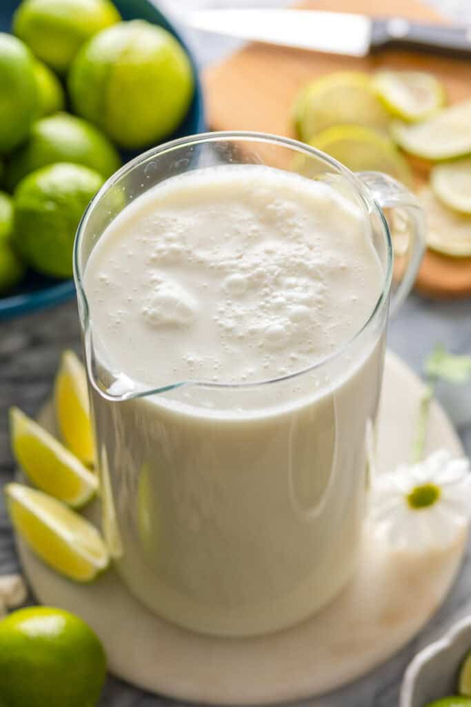 a pitcher full of Limonada Suíça also known as Brazilian Lemonade with fresh whole limes and sliced limes in surrounding