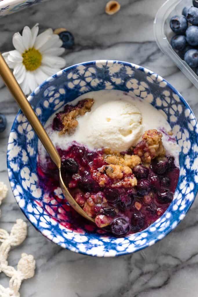 Gluten Free Blueberry Crumble in a bowl with a spoon and a scoop of vanilla ice cream 