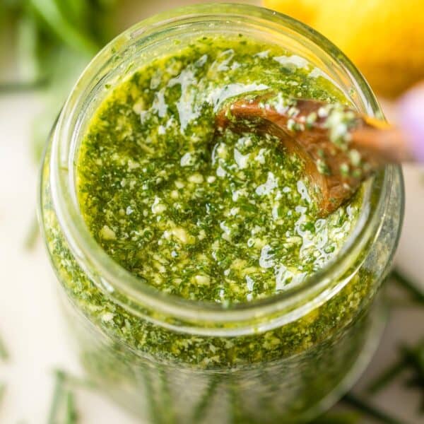 low fodmap pesto made with chives, basil, lemon and olive oil in a jar surrounded by fresh ingredients