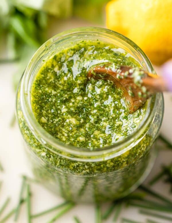 low fodmap pesto made with chives, basil, lemon and olive oil in a jar surrounded by fresh ingredients