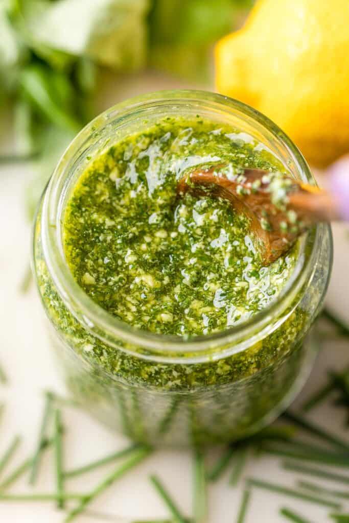 low fodmap pesto made with chives, basil, lemon and olive oil in a jar surrounded by fresh ingredients