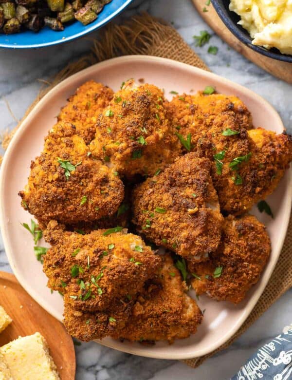 Oven Fried Chicken Thighs on a plate with fresh parsley on top with roasted okra, mashed potatoes and cornbread on the side