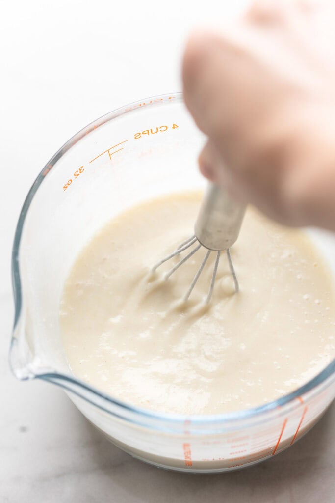 a measuring jug filled with a mixture of water and flour whisked together with text: 'whisk flour(s) + water'