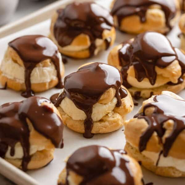 gluten free profiteroles on a baking sheet with freshly poured ganache on top