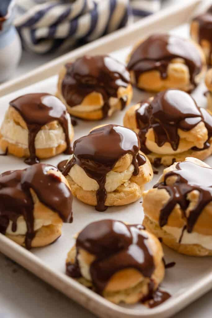 gluten free profiteroles on a baking sheet with freshly poured ganache on top