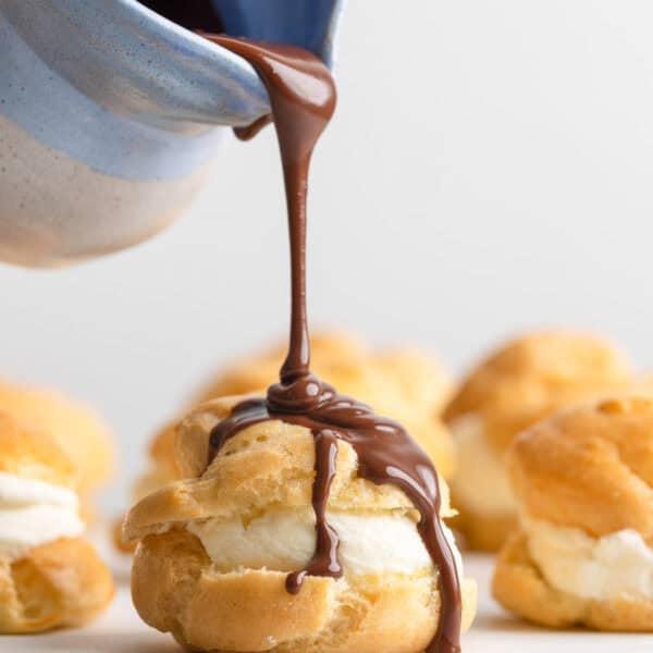 chocolate ganche pouring over a gluten free profiterole filled with mascarpone whipped cream