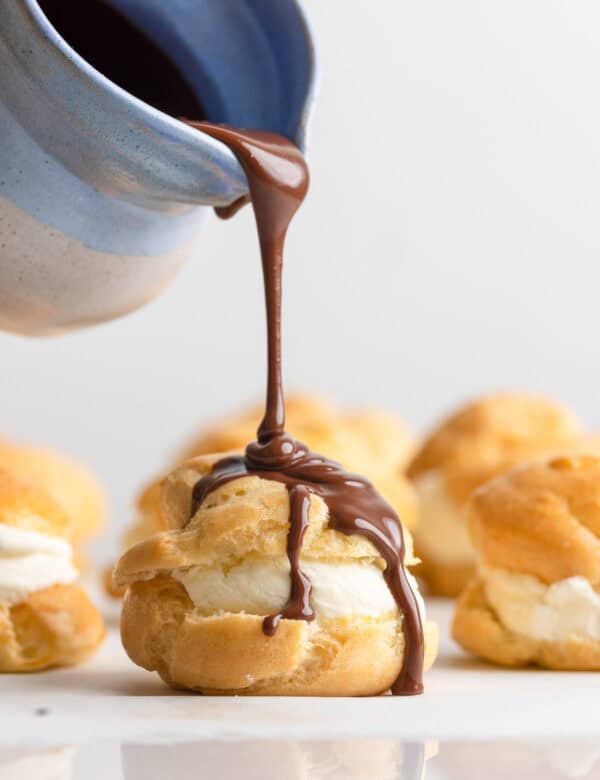 chocolate ganche pouring over a gluten free profiterole filled with mascarpone whipped cream