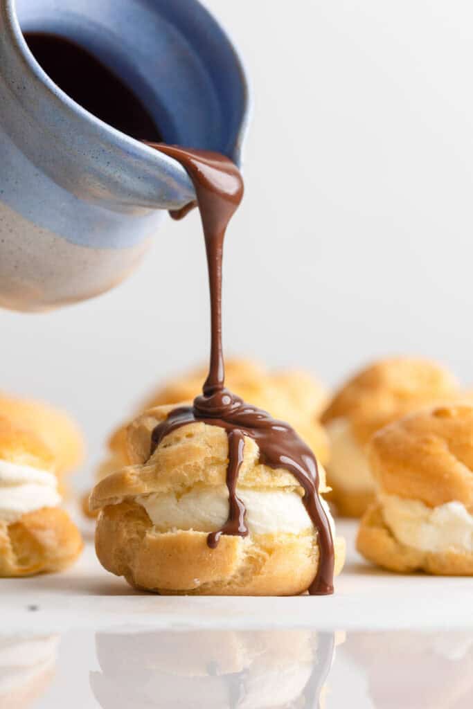 chocolate ganache pouring over a gluten free profiterole filled with mascarpone whipped cream