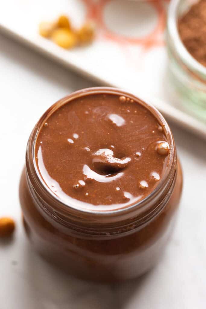 a jar full of homemade Nutella (chocolate hazelnut spread) with a loose hazelnut in the back