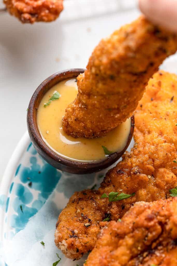 a chicken tender dipping into a small bowl of hot honey mustard dipping sauce