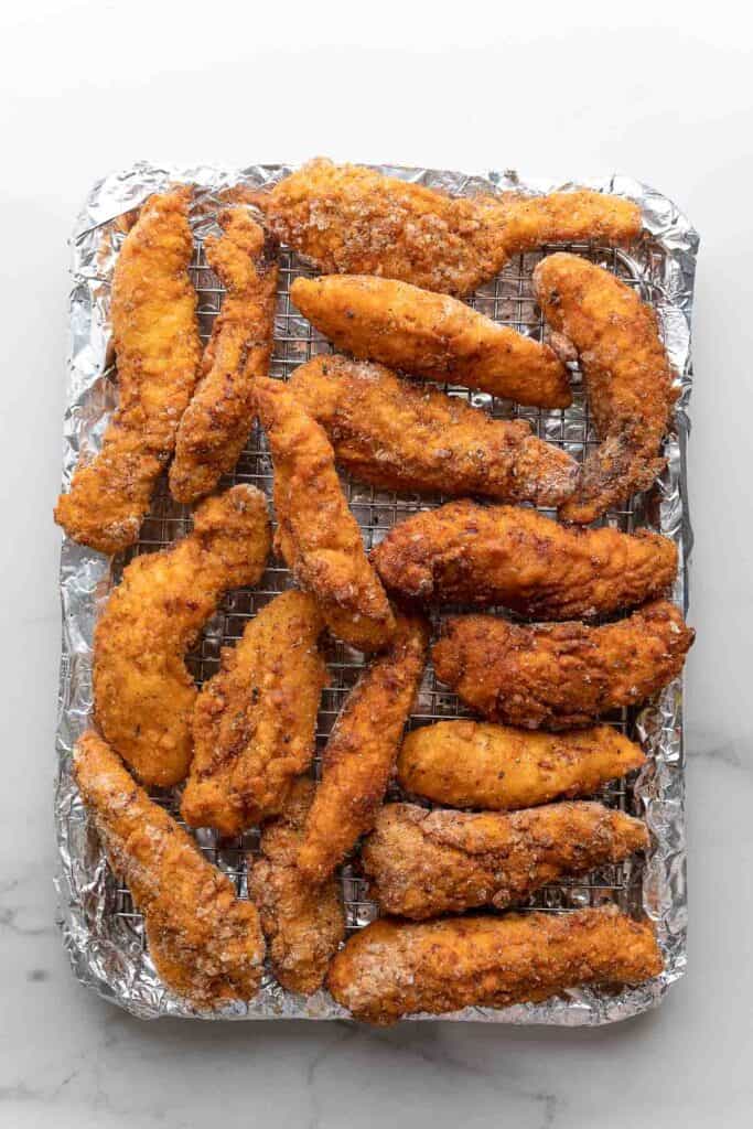 gluten free chicken tenders cooling on a wire rack over a baking sheet covered in foil