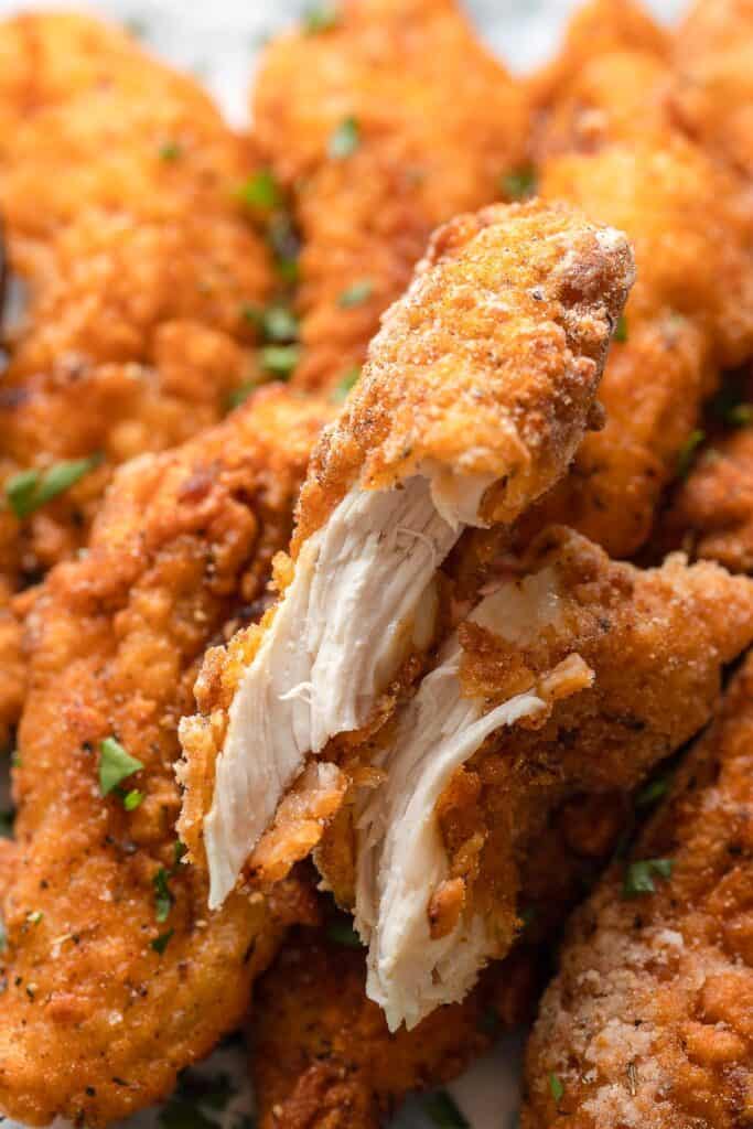 gluten free chicken tenders torn in half to show the juicy chicken on the inside