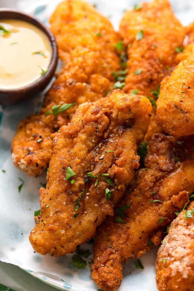 gluten free chicken tenders with fresh parsley sprinkled on top and a honey mustard dipping sauce on the side 