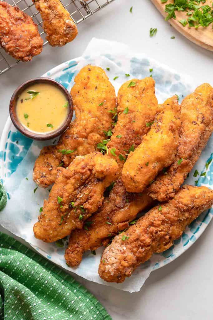 a plate full of gluten free chicken tenders with fresh parsley and a honey mustard dipping sauce on the side 