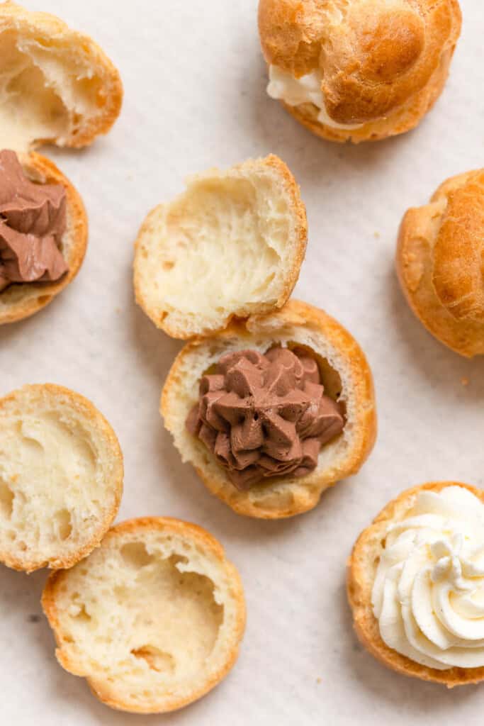 gluten free choux buns cut in half on a baking sheet - some are filled with chocolate mascarpone whipped cream and some with vanilla mascarpone whipped cream