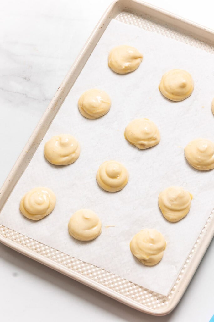 Gluten free choux batter piped on a tray. Text reads: 'smooth down tips (so they don't burn)