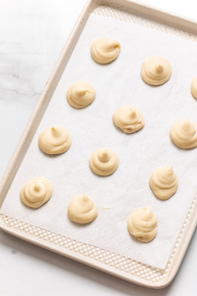 Gluten free choux batter piped on a tray. Text reads: 'pipe on prepped tray'