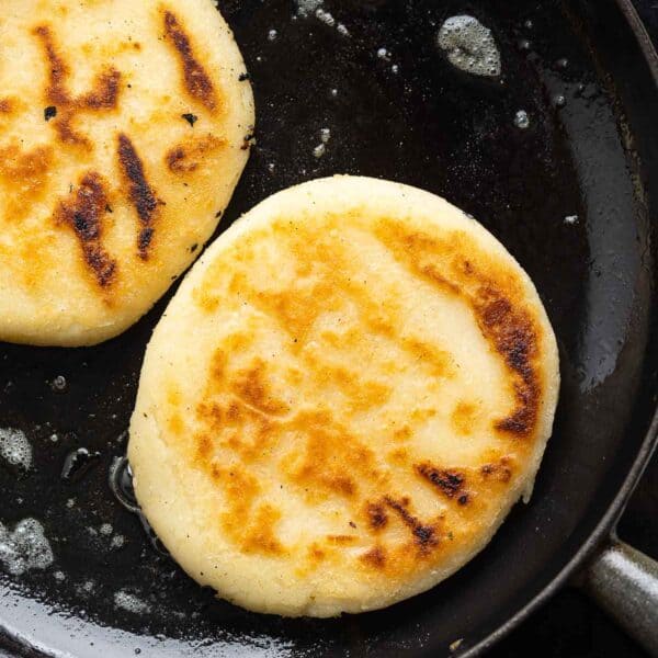 pan fried arepas in a cast iron skillet