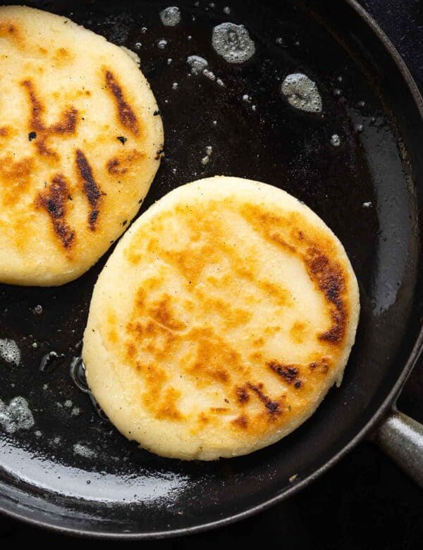 pan fried arepas in a cast iron skillet