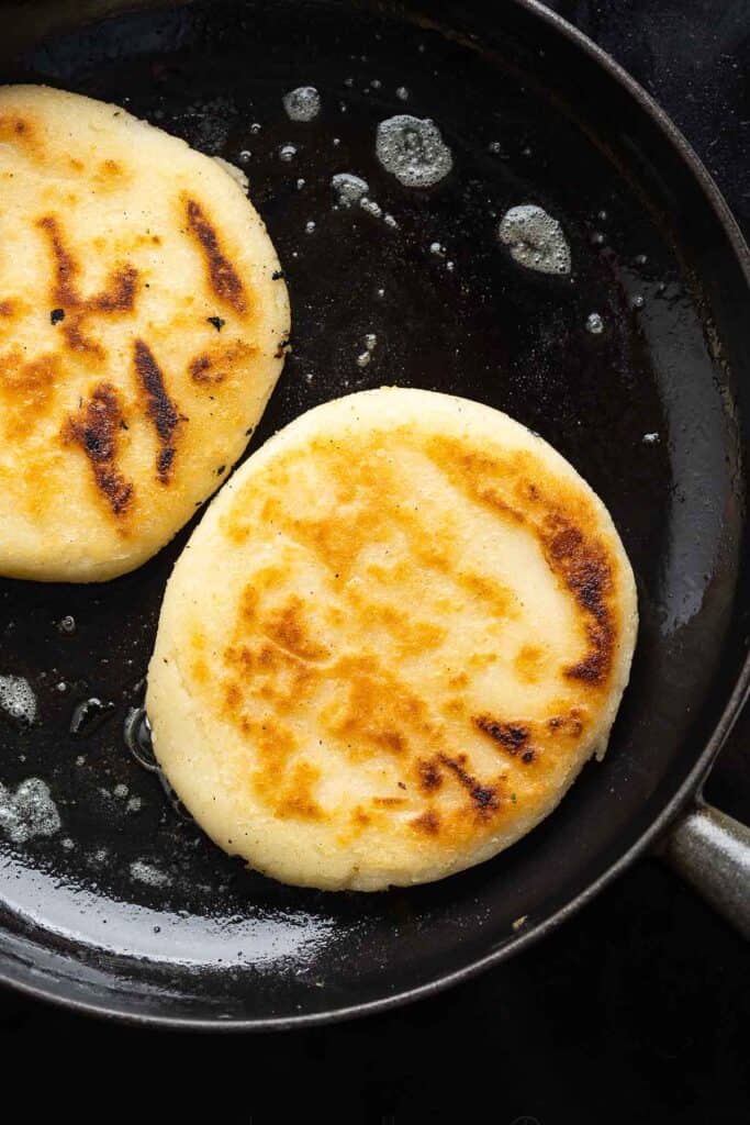 pan fried arepas in a cast iron skillet