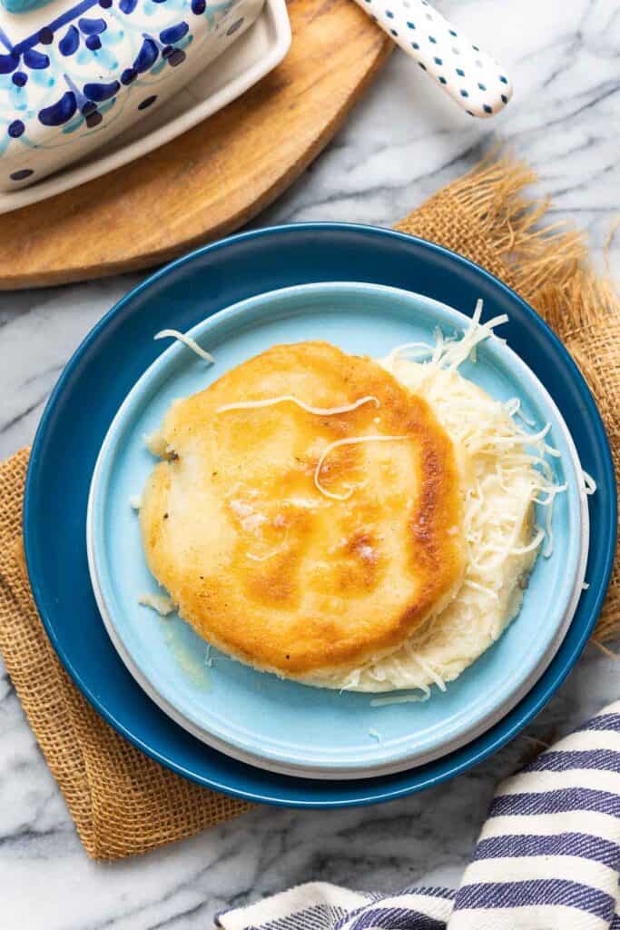 an arepa on a plate with shredded cheese in the middle