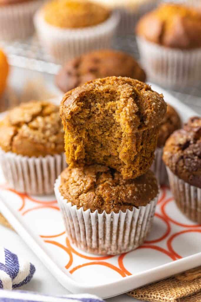 Gluten free pumpkin muffins on a plate - one muffin stack on top of another muffin. The top muffin has a bite taken out of it.