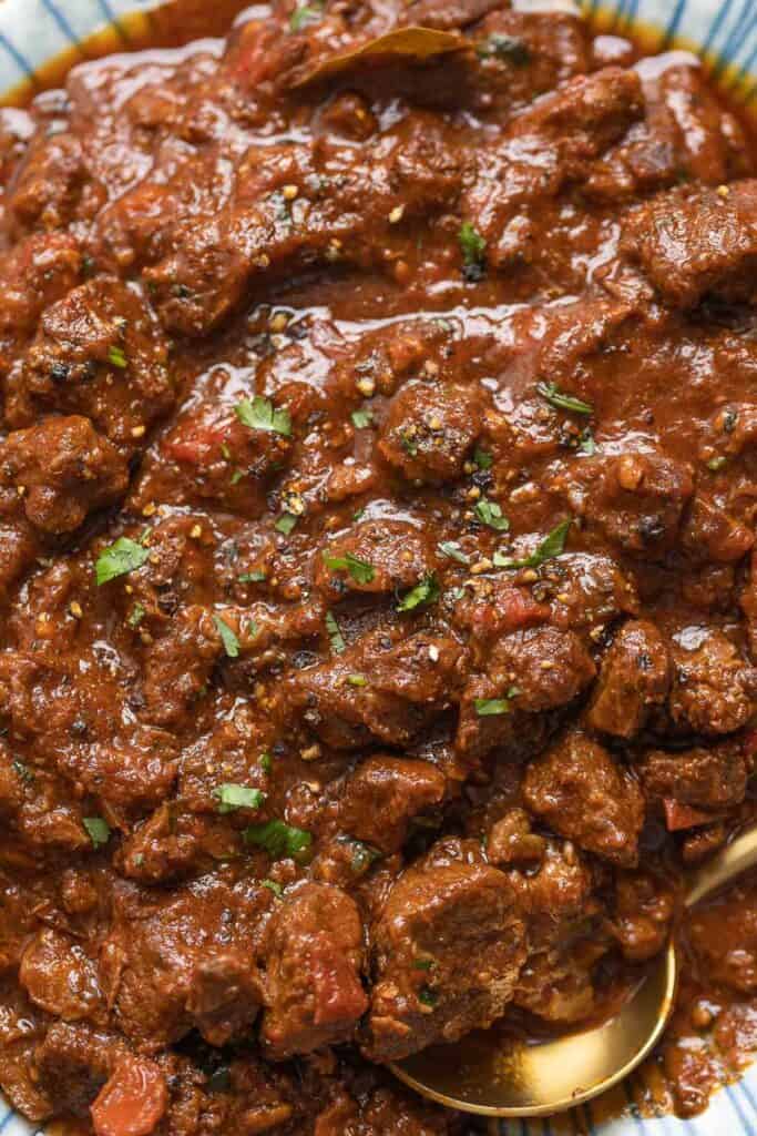 a bowl full of extra Saucy Carne Desmechada topped with chopped cilantro and fresh black pepper and serving spoon on side