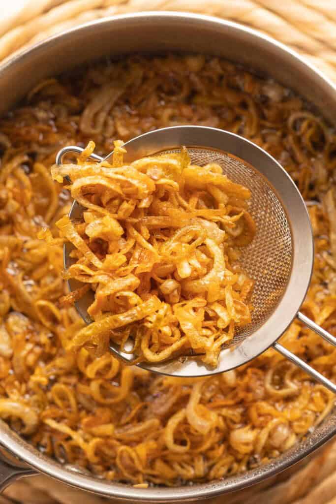 a fine mesh metal sieve removing crispy fried shallots from hot oil