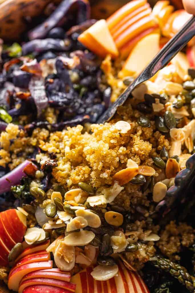 a pair of tongs mixing together a  salad made with Roasted Cabbage and Kale, Crispy Quinoa, apples, fried halloumi, pumpkin seeds and almond slices