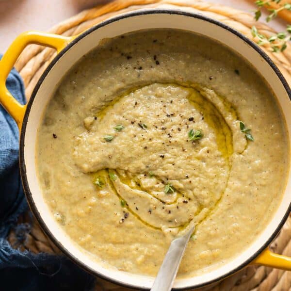 Roasted Cauliflower and Garlic Soup in a soup pot with a ladle topped with an olive oil dried and fresh thyme leaves