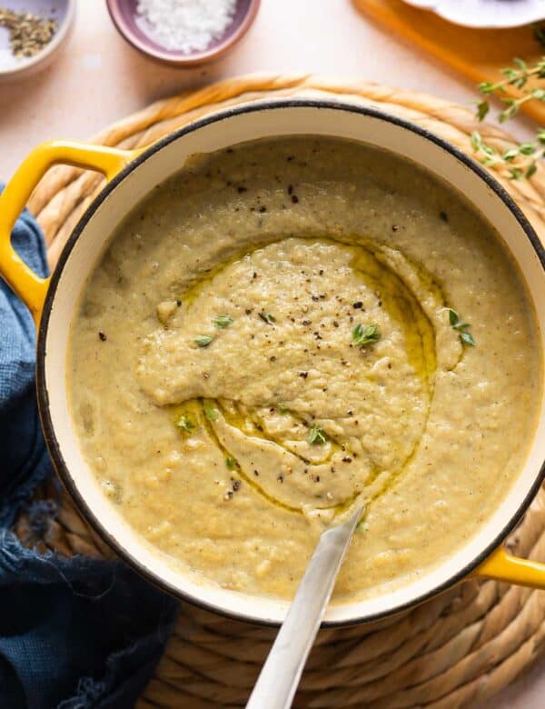 Roasted Cauliflower and Garlic Soup in a soup pot with a ladle topped with an olive oil dried and fresh thyme leaves