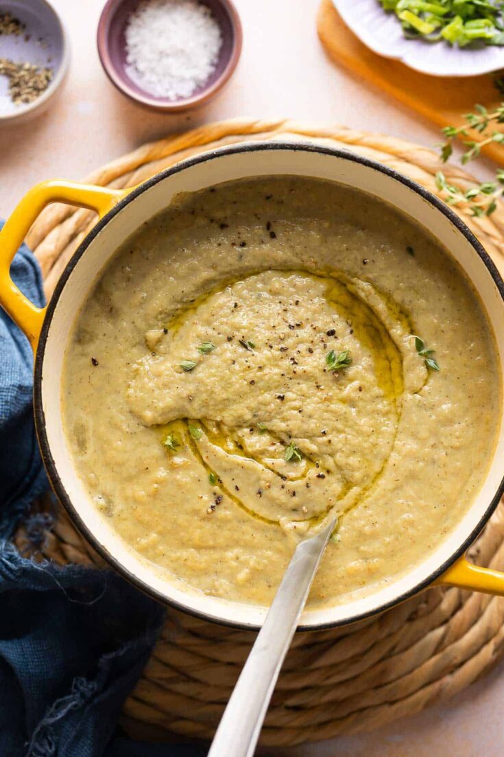 Roasted Cauliflower and Garlic Soup in a soup pot with a ladle topped with an olive oil dried and fresh thyme leaves