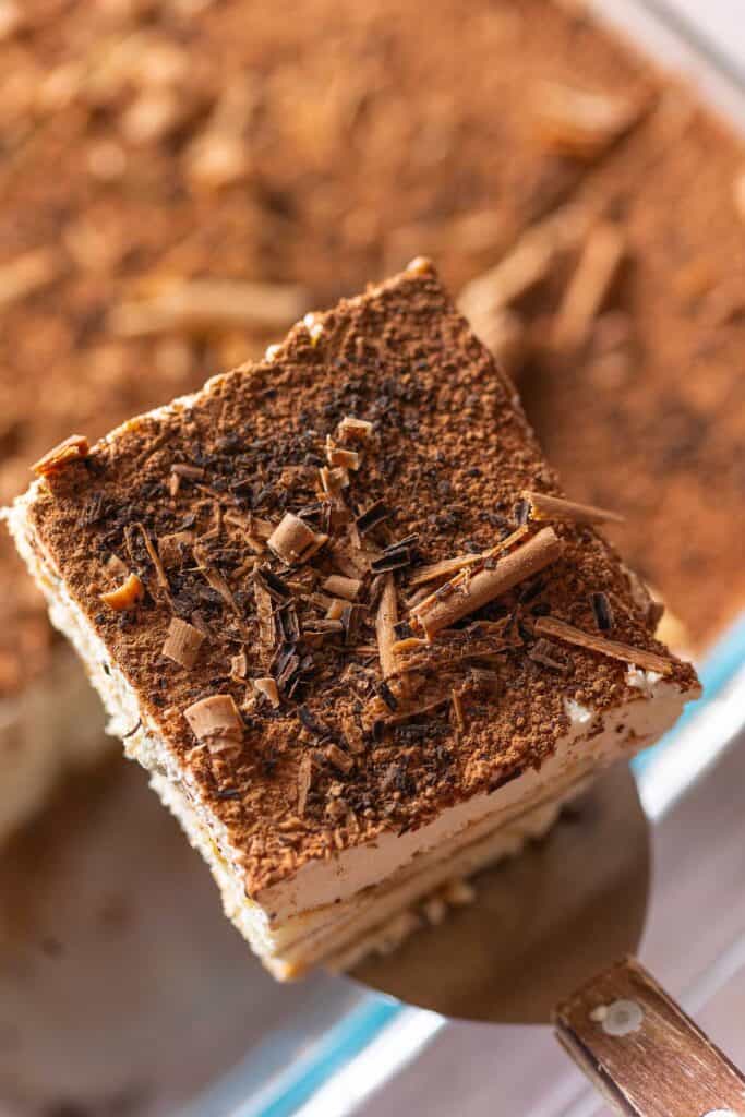 a slice of tiramisu covered in cocoa powder and chocolate shavings on a spatula 