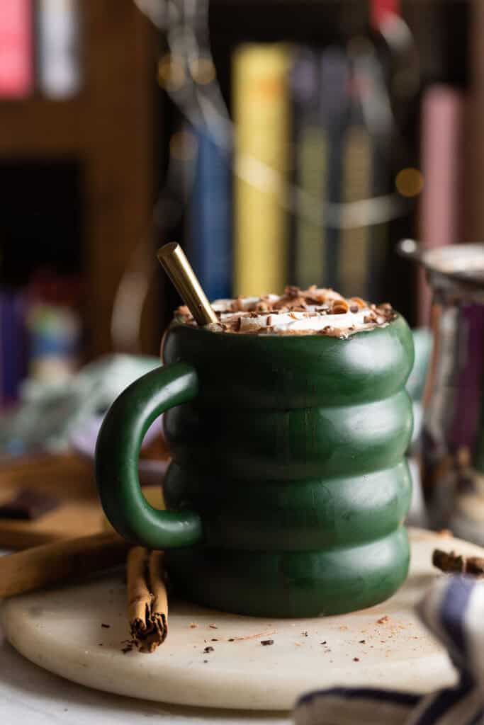 a mug of chai hot chocolate with whipped cream and cinnamon on top with cinnamon sticks on the side