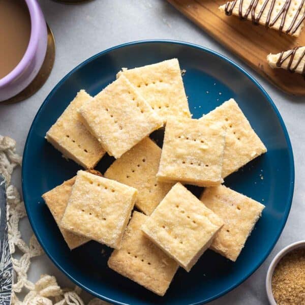 Gluten Free Shortbread cut into squares on a plate with some shortbread cookies cut into triangles and drizzled with chocolate and a couple mugs on coffee on the side