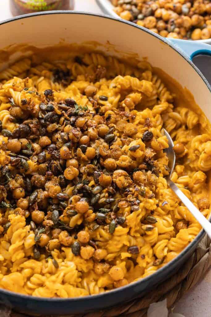 Creamy Roasted Butternut Squash Pasta in a large dish topped with fried chickpeas and pepitas (hulled pumpkin seeds) scooped up on a serving spoon.