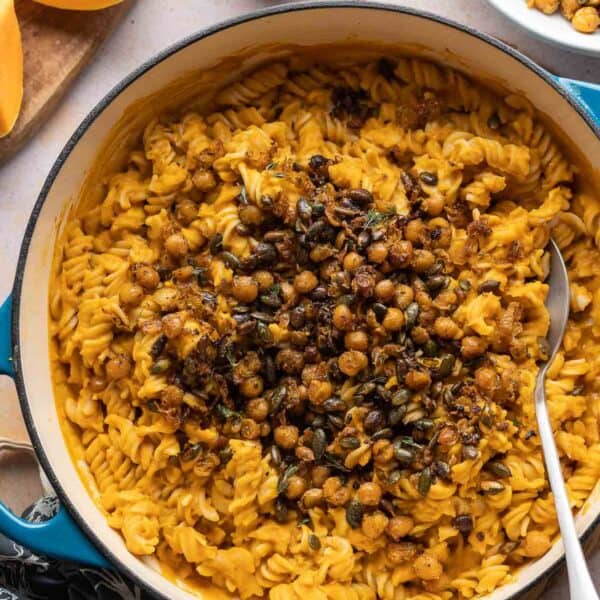 A large pan full of gluten free fusilli mixed in a vegan roasted butternut squash sauce and topped with fried chickpeas and pumpkin seeds.