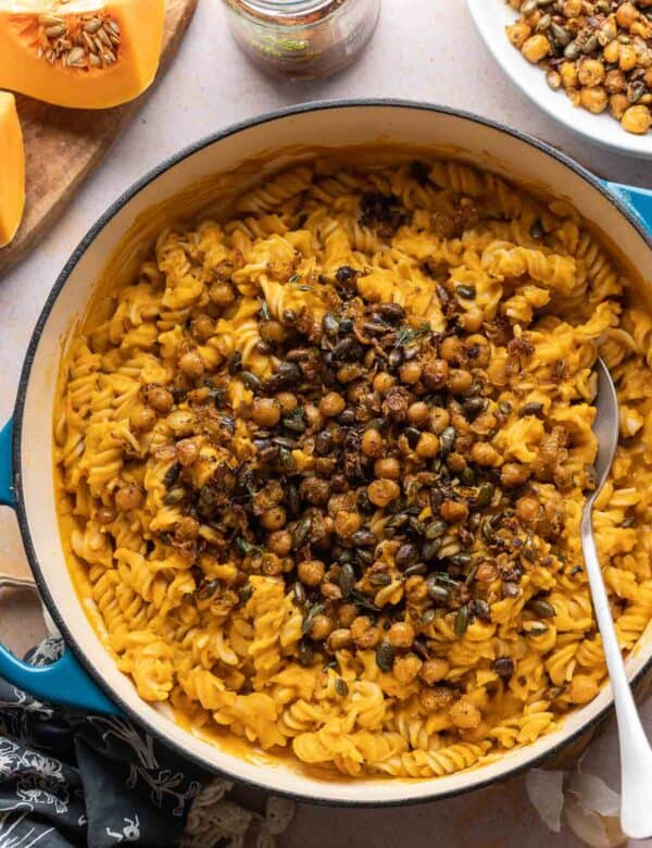 A large pan full of gluten free fusilli mixed in a vegan roasted butternut squash sauce and topped with fried chickpeas and pumpkin seeds.