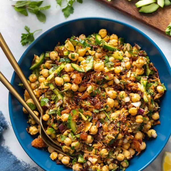 A salad bowl full of a Crispy Rice Salad with Lemony Chickpeas & Cucumber with fresh herbs, diced cucumber and lemon wedges around the bowl.