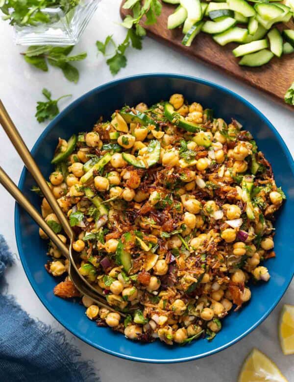 A salad bowl full of a Crispy Rice Salad with Lemony Chickpeas & Cucumber with fresh herbs, diced cucumber and lemon wedges around the bowl.