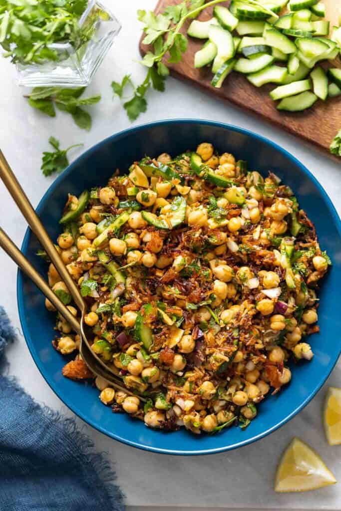 A salad bowl full of a Crispy Rice Salad with Lemony Chickpeas & Cucumber with fresh herbs, diced cucumber and lemon wedges around the bowl.